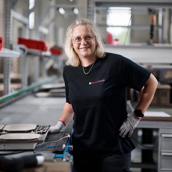 Eine Frau in einem schwarzen Shirt steht in einer Produktionsstätte.