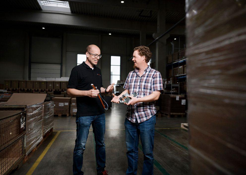 Zwei Männer stehen in einem Lager und unterhalten sich